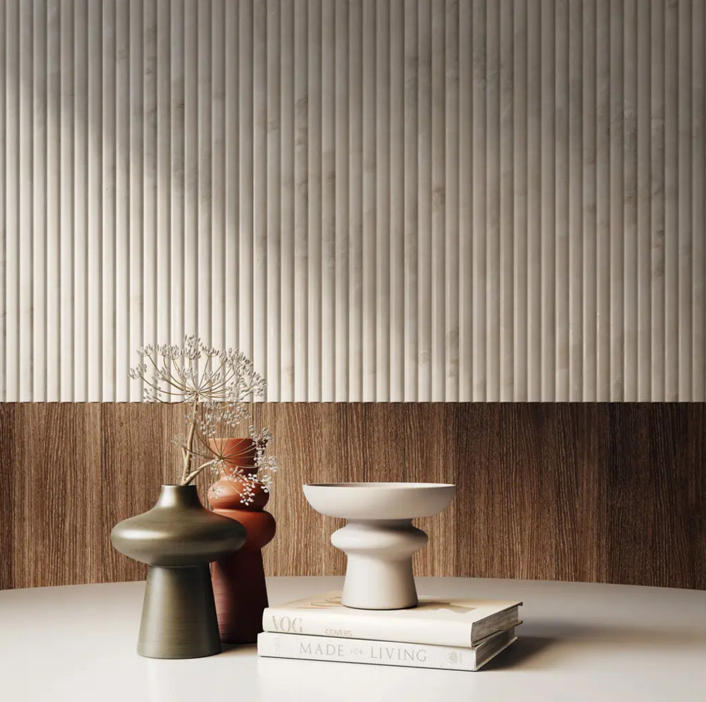 Nowoczesna minimalistyczna ekspozycja z rzeźbionymi wazonami, białą misą, suszonymi kwiatami i ułożonymi książkami na białej powierzchni - odzwierciedlająca porządek centralizacji danych produktowych PIM - ustawiona na tle teksturowanej ściany z pionowymi wypukłościami i drewnianymi panelami.